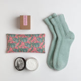 A pair of peppermint angora socks are paired with a floral eye pillow, rich moisturizer in vintage peony and a natural candle infused with tuberose and orange peel.
