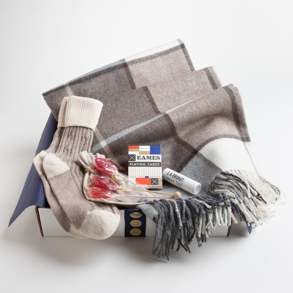 A luxe alpaca blanket, cashmere mix slouch socks, organic lip balm, and a deck of playing cards designed in tribute to Ray and Charles Eames provide a true at-home oasis.