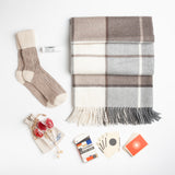 A luxe alpaca blanket, cashmere mix slouch socks, organic lip balm, and a deck of playing cards designed in tribute to Ray and Charles Eames provide a true at-home oasis.