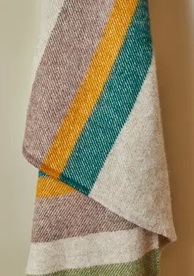 Close up of pure new wool throw in a rich multistripe of olive, mustard, emerald green, and camel on a natural beige background.