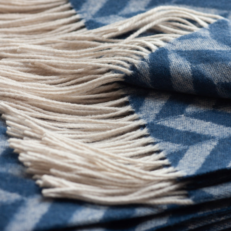 Close-up of a lambswool throw blanket with cream-colored fringe and a blue and white herringbone pattern.
