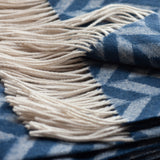 Close-up of a lambswool throw blanket with cream-colored fringe and a blue and white herringbone pattern.