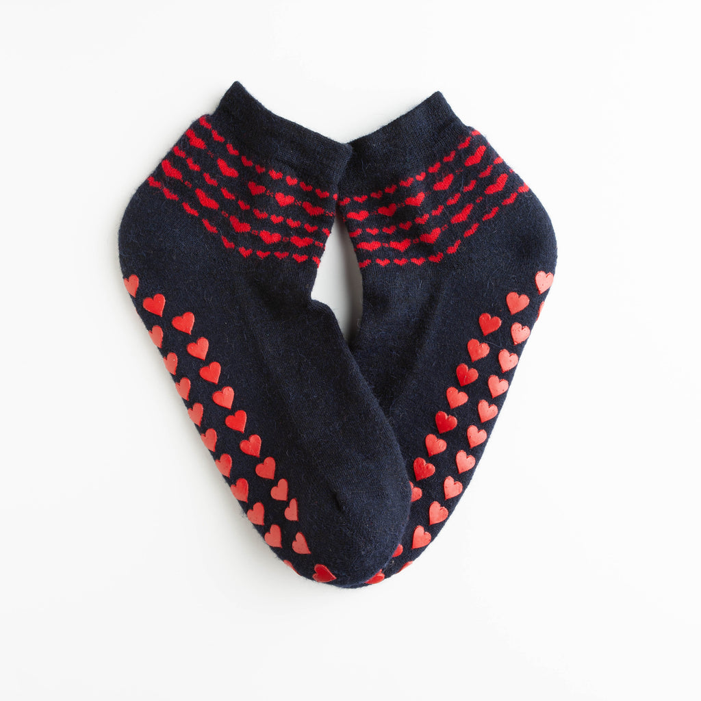 Navy slipper socks with red non-slip hearts are a cozy blend of alpaca, wool, and acrylic. Terry-cushioned soles provide extra comfort. Made in Peru.