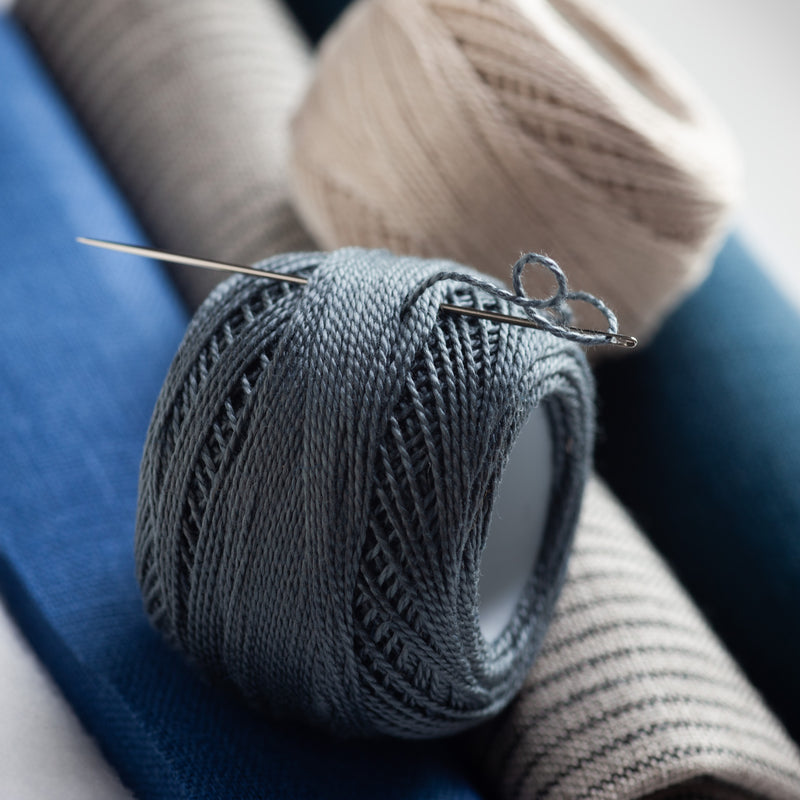 Close-up of gray and cream spools of Perle cotton thread.