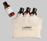 LA Bruket Discovery Kit containing four small amber bottles of body wash, hand wash , shampoo and conditioner in a branded natural linen bag. w