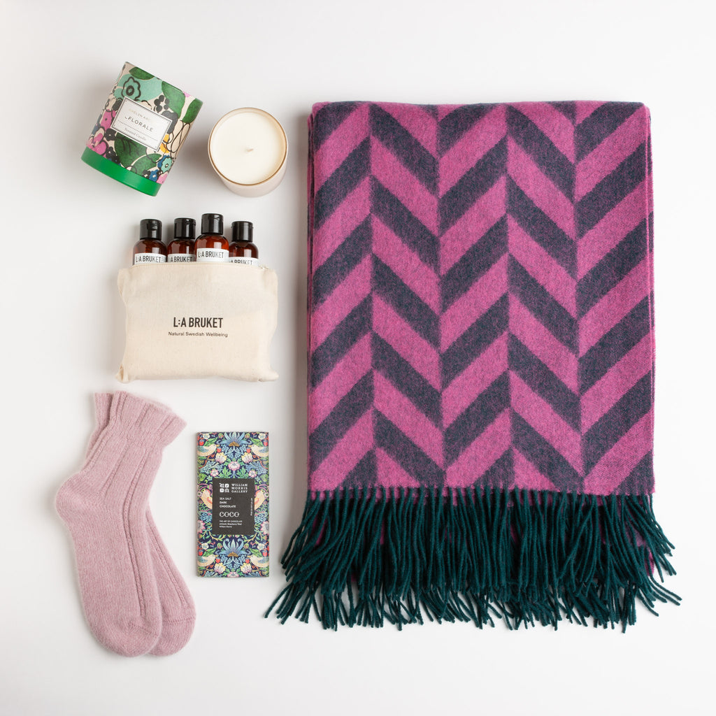 A lively pink and emerald lambswool throw, angora bed socks, a sea salt dark chocolate bar, a floral scented candle, and an LA Bruket organic skincare travel kit.