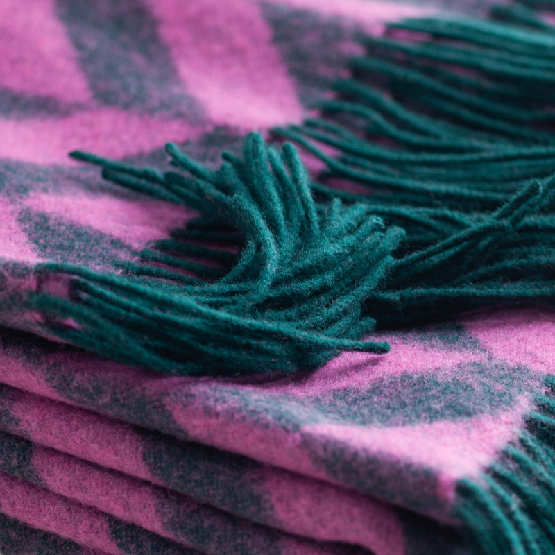 A folded chrevron-patterned  throw in vibrant pink and emerald green with emerald green fringe.
