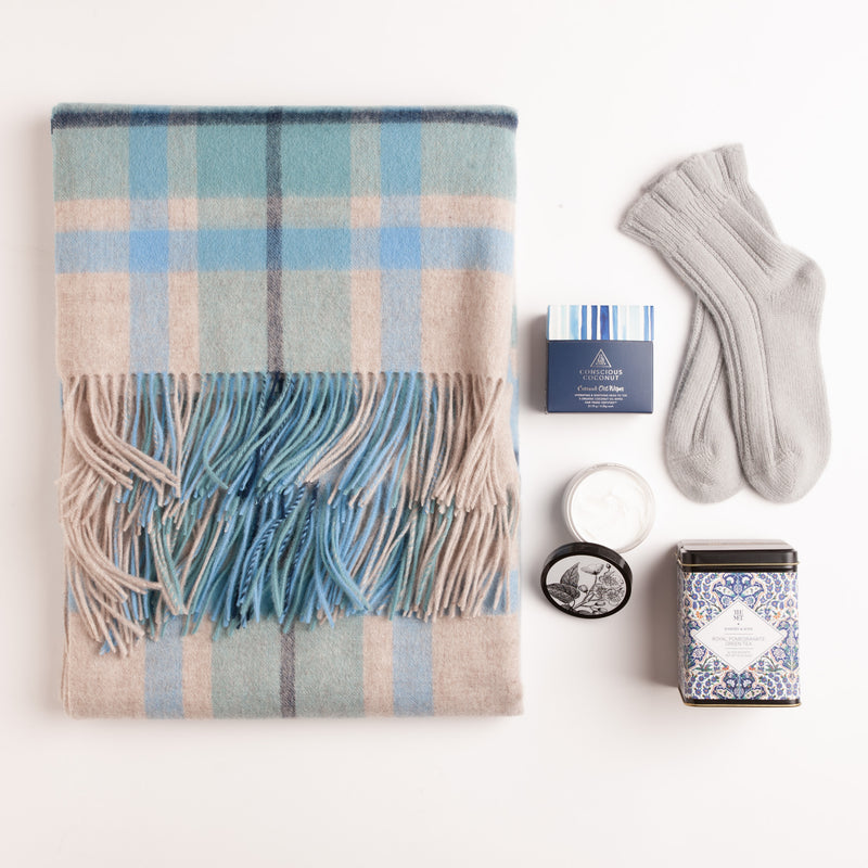 This gift is designed to envelop the receiver in blissful comfort. It includes a lovely lambswool throw, cozy angora socks, a nourishing hand and body cream, and refreshing pomegranate green tea, making it an ideal companion for peaceful moments at home.
