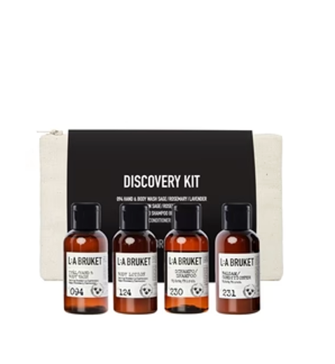 LA Bruket Discovery Kit containing four small amber bottles of body wash and hand wash with black caps, displayed in front of a black and white branded box.