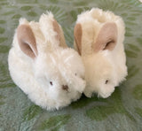 Pair of plush baby bunny slippers on blanket background.