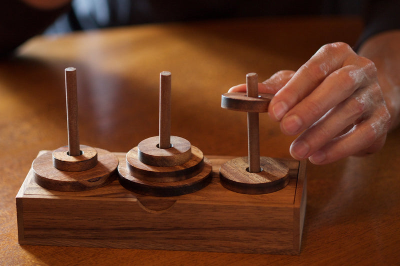 Tower of Hanoi wooden puzzle with person interacting with it.