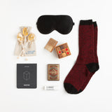 Soft but rugged alpaca socks, a black silk eye mask, moisturizing lip balm, and a regal deck of playing cards are the perfect wellness accessories for lounging around in style.