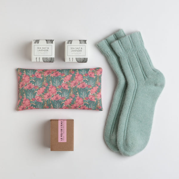 A pair of  peppermint angora socks are paired with a matching floral eye pillow. They are accompanied by two sparkling bath tablets and a3 oz. natural candle infused with tuberose and orange peel.