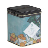 A square metal tea tin with a black lid and a printed label showing fruit and a blue-toned background. The front label reads 'THE MET HARNEY & RINS HOT APPLE SPICE BLACK TEA'.